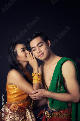 Beautiful young Thai woman hand up whisper man wearing elegant traditonal performance colorful dress with jewelry on black background, Isolated.