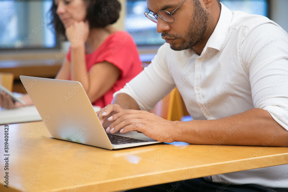 Cropped shot of focused man typing on laptop. Handsome young student sitting at library and using modern device. Technology concept Cropped shot of focused man typing on laptop. Handsome young student sitting at library and using modern device. Technology concept