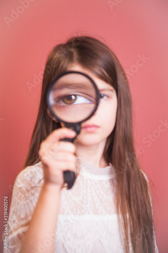 a beautiful girl in a white dress plays with a magnifying glass on a pink background