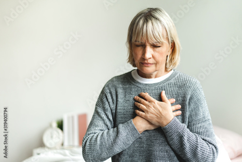 Senior adult elderly women sit on bed with chest pain suffering from heart attack in the bedroom.Healthcare and medical concept photo