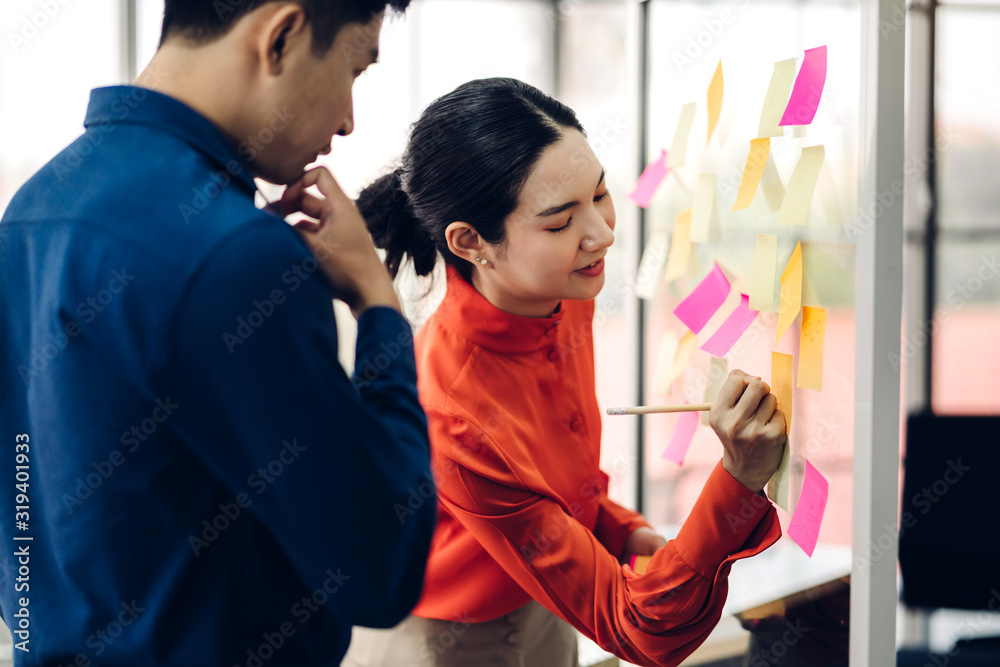 Two casual business people planning and brainstorm writing over the project with stickers note on glass window at modern office.Teamwork concept Two casual business people planning and brainstorm writing over the project with stickers note on glass window at modern office.Teamwork concept
