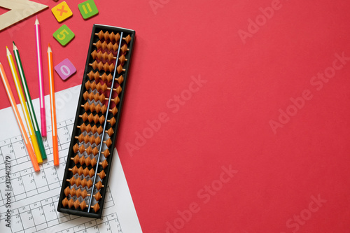 Mental arithmetic and math concept: colorful pens and pencils, numbers, abacus scores on red background, copy space