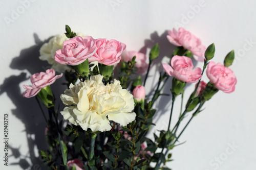 Super cute, light color flower bouquets including baby pink and white dianthus flowers with white chrysanthemum flowers, and some other white flowers. Photographed with a white wall on the background. © Nora