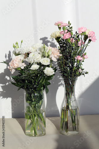 Super cute  light color flower bouquets including baby pink and white dianthus flowers with white chrysanthemum flowers  and some other white flowers. Photographed with a white wall on the background.