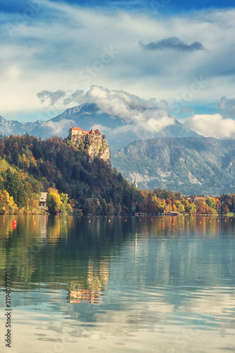 Famous alpine Bled lake (Blejsko jezero) in Slovenia, amazing autumn landscape. Aerial view of the lake, Bled castle, mountains and blue sky with clouds, outdoor travel vertical background