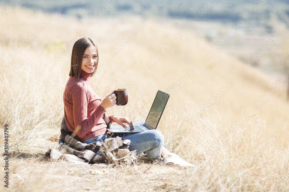 Young attractive woman working on laptop outdoors. Woman on natural background doing her freelance job on pc. Remote vorker on vacation.