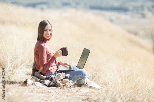 Young attractive woman working on laptop outdoors. Woman on natural background doing her freelance job on pc. Remote vorker on vacation.