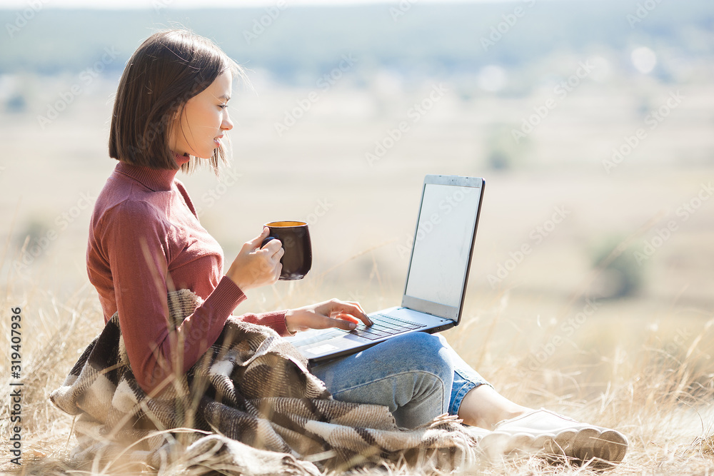 Young attractive woman working on laptop outdoors. Woman on natural background doing her freelance job on pc. Remote vorker on vacation.