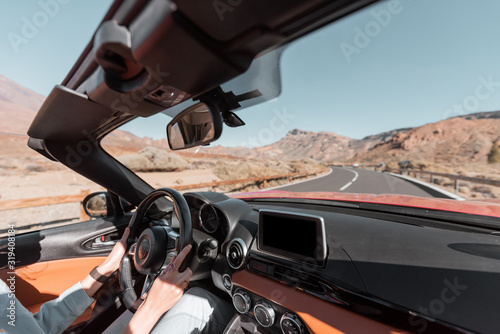Woman driving car on the desert road, close-up view focused on the steering wheel and hands. Beautiful road on the volcanic valley