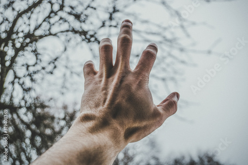 male left hand reaching for dark blue sky with copy space for text. point view shot of human hand. Color toned image. Concept of religion, freedom, help,dream.