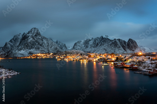 Winter panorama of Reine village at night and outstanding snowy mountains on horizon. Lofoten islands, Norway.