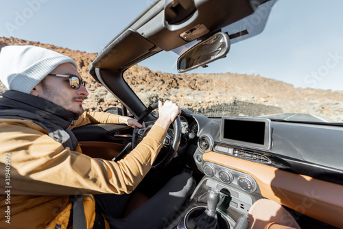 Man driving convertible car while traveling on the desert road. Carefree lifestyle and travel concept