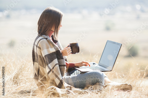 Young attractive woman working on laptop outdoors. Woman on natural background doing her freelance job on pc. Remote vorker on vacation. photo