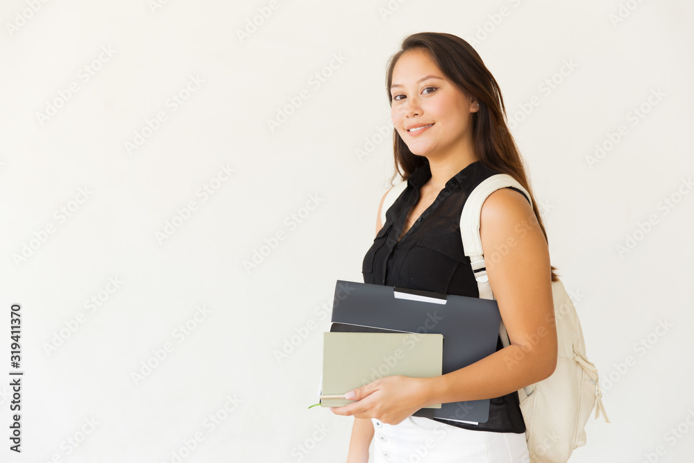 Happy female student with folder and books. Side view of cheerful young woman with backpack holding textbooks with pen and smiling at camera isolated on white background. Education concept Happy female student with folder and books. Side view of cheerful young woman with backpack holding textbooks with pen and smiling at camera isolated on white background. Education concept