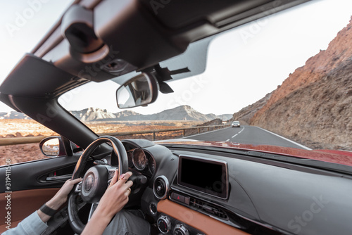 Woman driving car on the desert road, close-up view focused on the steering wheel and hands. Beautiful road on the volcanic valley © rh2010