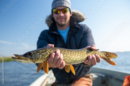 Young fisherman holds the pike fish