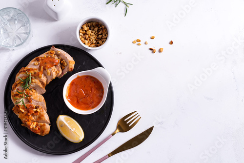 Grilled chicken breast with sauce, peanuts and lemon on a plate on stone background
