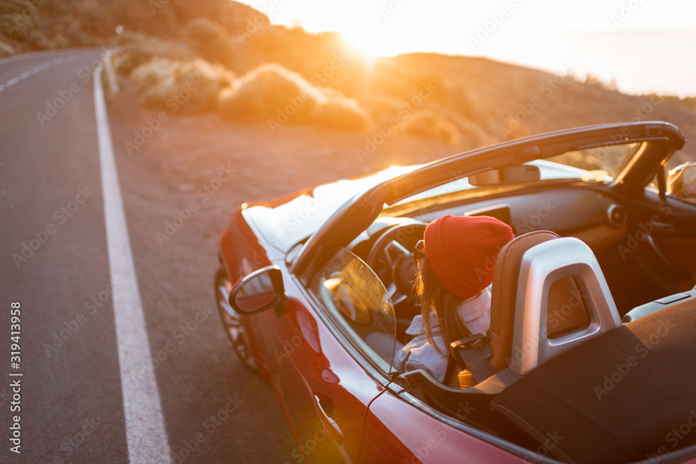 Young woman traveling by car on a beautiful mountain road during a sunset