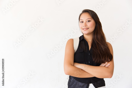 Content young woman with backpack looking at camera. Portrait of beautiful happy young female college student standing with crossed arms and looking at camera. Education concept
