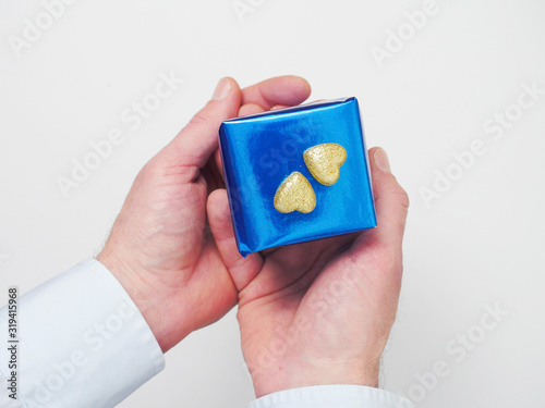 Man holding blue gift box with two golden hearts on top of the box with his two hands. Concept Saint Valentine gift and a way to say I love you.