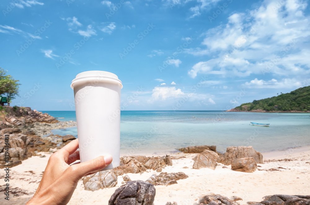 Hand holds a white cardboard paper mug for takeaway drinks, against beautiful sea shore background, environment concept, mock up Hand holds a white cardboard paper mug for takeaway drinks, against beautiful sea shore background, environment concept, mock up