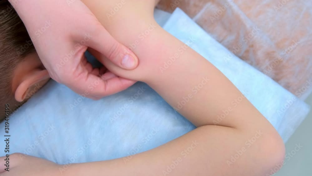 Doctor massagist making therapeutic massage to teen boy on shoulder in clinic, closeup view. Child boy lying on couch. Cure massage, rehabilitation after injury. Medicine treatment for children. Doctor massagist making therapeutic massage to teen boy on shoulder in clinic, closeup view. Child boy lying on couch. Cure massage, rehabilitation after injury. Medicine treatment for children.