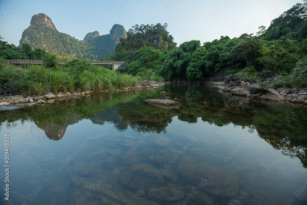 Calm river with mountains on the horizon and woman sitting on the rock (at right) Calm river with mountains on the horizon and woman sitting on the rock (at right)
