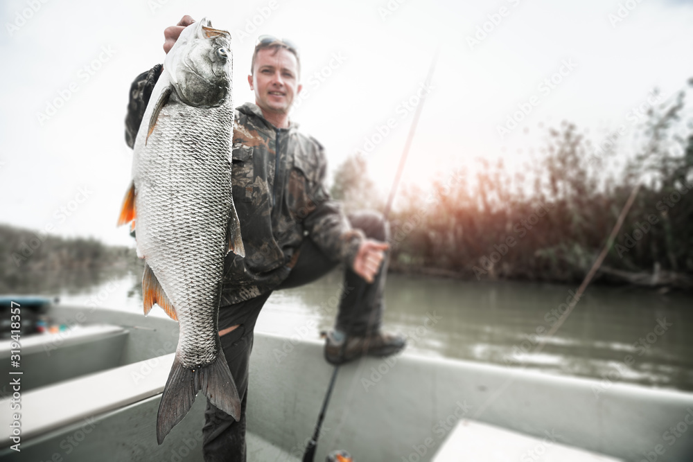 Amateur angler stands in the boat and holds the trophy Asp fish (Leuciscus aspius) with natural background. Tilt shift effect applied, image is blurred, focus on the fish only. Amateur angler stands in the boat and holds the trophy Asp fish (Leuciscus aspius) with natural background. Tilt shift effect applied, image is blurred, focus on the fish only.