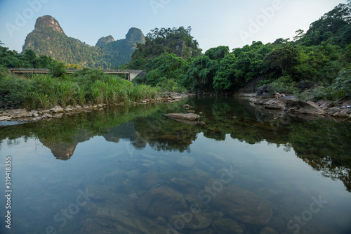 Calm river with mountains on the horizon and woman sitting on the rock (at right)