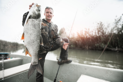 Amateur angler stands in the boat and holds the trophy Asp fish (Leuciscus aspius) with natural background. Tilt shift effect applied, image is blurred, focus on the fish only.