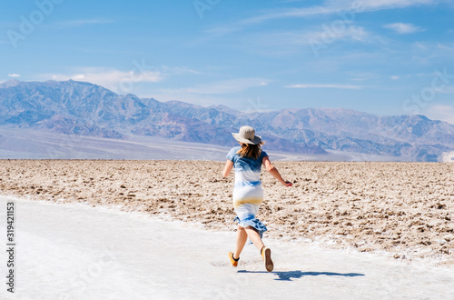 A beautiful woman with hat and summer dress in white and yellow blue walks runs jumps and enjoys the desert landscape of Death Valley in California USA