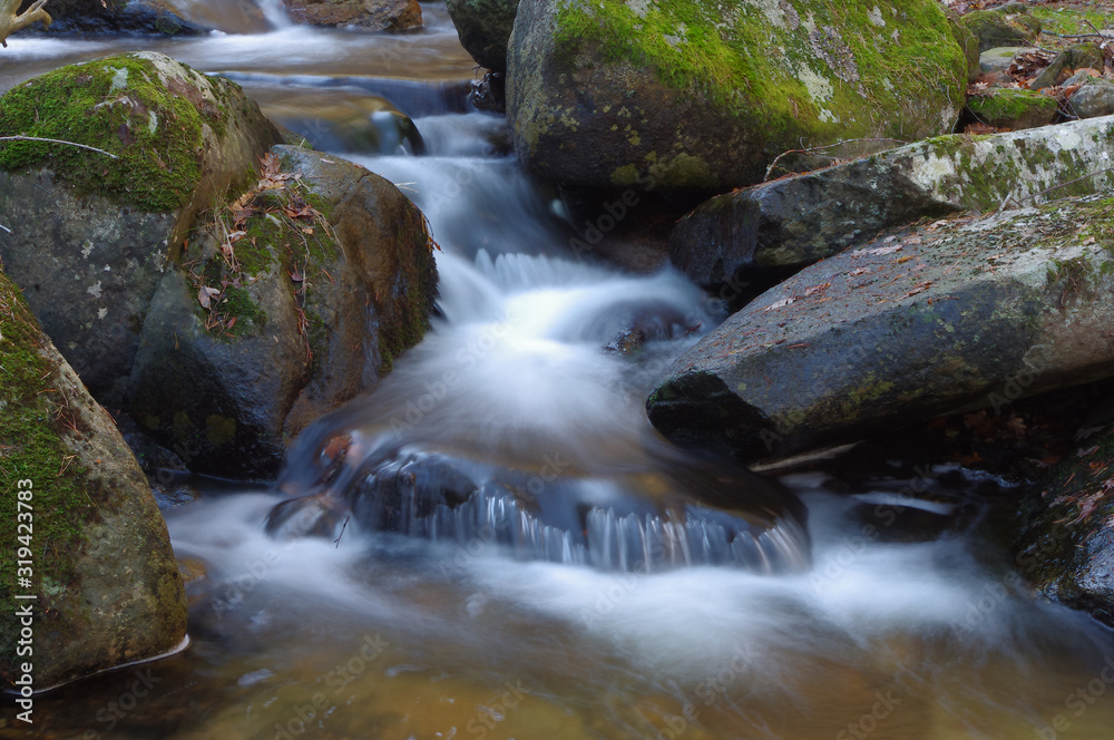 Water falls with movement effect on a river in winter with a blanket of dried leaves, Lozoya Valley, Madrid, Spain Water falls with movement effect on a river in winter with a blanket of dried leaves, Lozoya Valley, Madrid, Spain