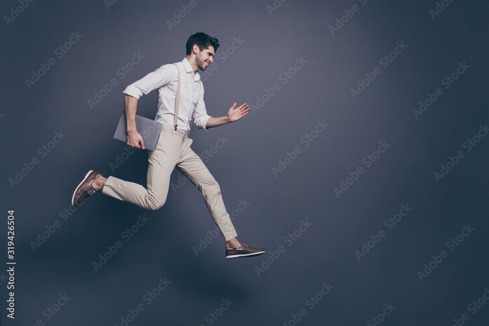 Full length profile side photo of cheerful excited guy hold computed know information about black friday discounts jump run fast wear modern clothing isolated over grey color background
