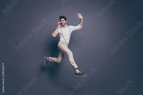 Full length photo of cheerful girl relax speak smartphone girlfriend look friend hold hand greet scream hi jump run fast hurry wear white shirt pants trousers isolated grey color background