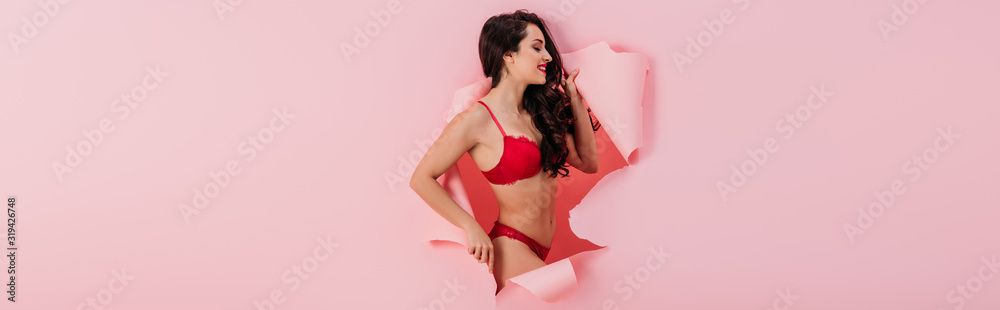 panoramic shot of sexy girl in red lingerie standing in paper hole on pink background - obrazy, fototapety, plakaty 