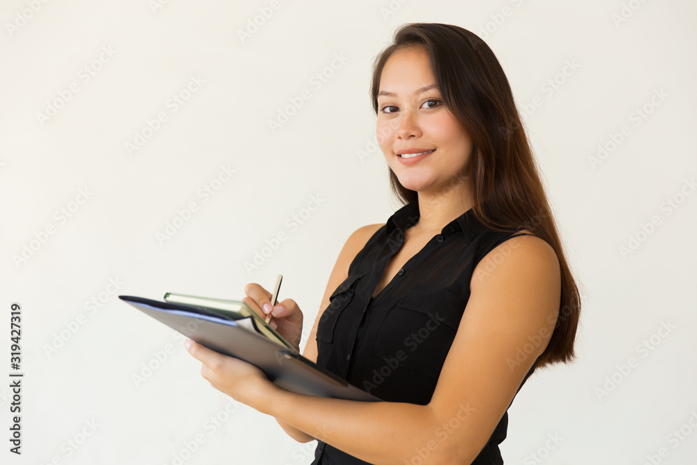 Content student writing and smiling at camera. Beautiful happy young Asian woman holding folder, book and pen isolated on white background. Education concept Content student writing and smiling at camera. Beautiful happy young Asian woman holding folder, book and pen isolated on white background. Education concept