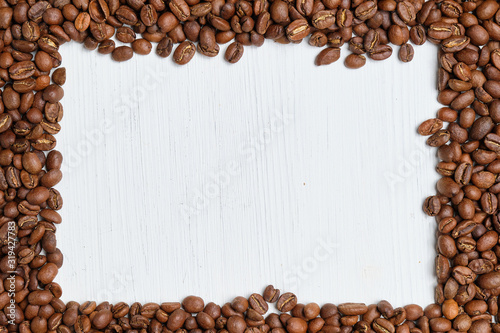 A frame of roasted coffee beans on a white wooden background. Copy space. Top view.