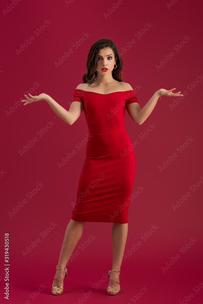 displeased elegant girl looking at camera while standing with open arms isolated on red displeased elegant girl looking at camera while standing with open arms isolated on red