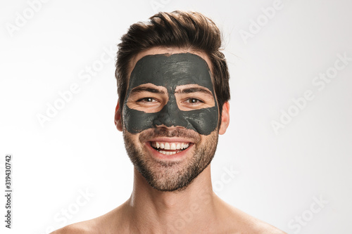 Photo of happy half-naked man with cosmetic mask on his face smiling