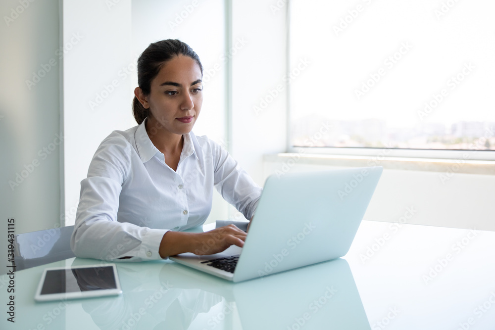 Serious young businesswoman using laptop in office. Focused young businesswoman sitting at desk and using laptop computer in modern office. Business and technology concept Serious young businesswoman using laptop in office. Focused young businesswoman sitting at desk and using laptop computer in modern office. Business and technology concept