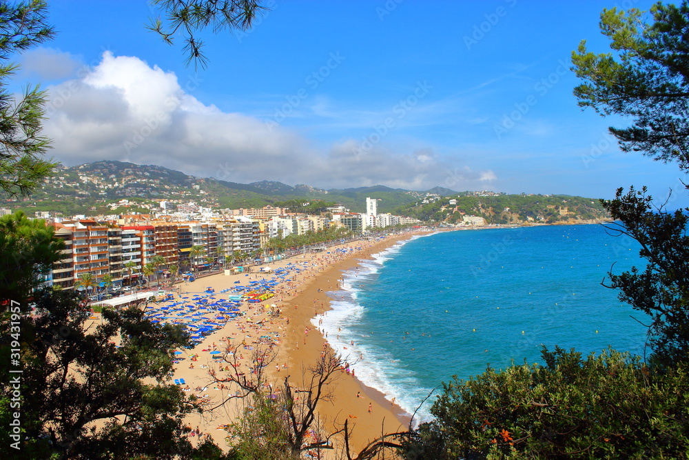 View of the blue sea, beach, yellow sand, the resort town and green mountains against the blue sky and white clouds.