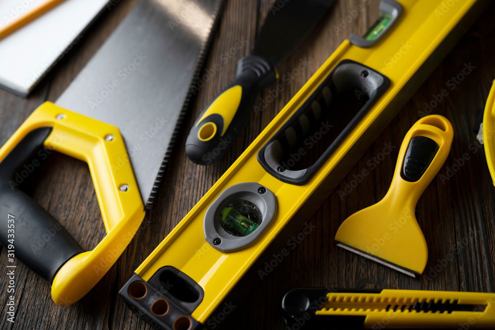 Contractor concept. Tool kit of the contractor: yellow hardhat, libella, hand saw, and notebook on the rustic wooden background.