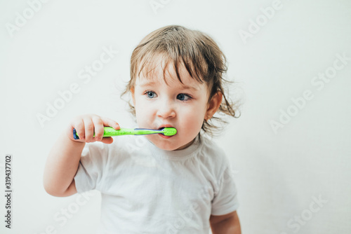 Little girl brushes her teeth with a toothbrush on a light background