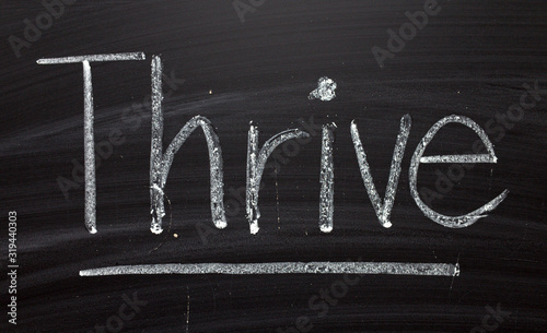 The word Thrive written by hand in white chalk on a blackboard as a reminder