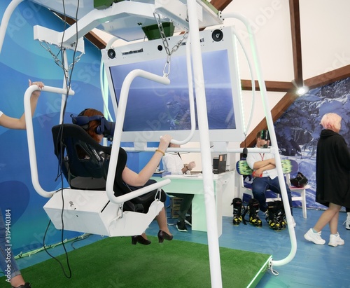 A girl on a virtual hang glider ride sits in a virtual reality helmet under the control of an operator. New technologies in flight training.