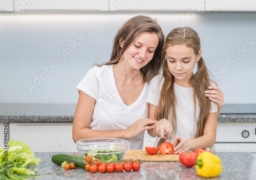 Happy family at home. Mother teaches her daughter to cut vegetables for dinner. Empty space for text