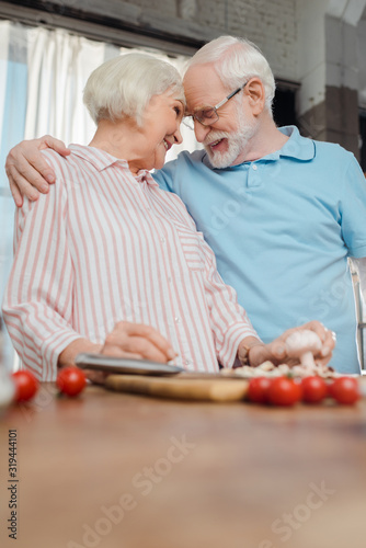 Selective focus of smiling man hugging wife by vegetables and cutting board on kitchen table