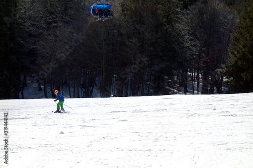 Kind fährt ski auf beschneiter weiser skipiste im schwarzwald am feldberg. oben fährt ein sessellift. photo