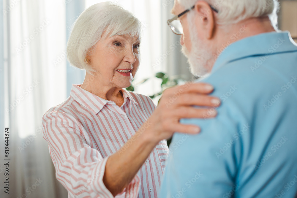 Selective focus of smiling senior woman embracing husband at home