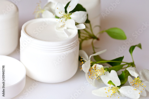 Close up view on a white jar with cosmetic for face care and apple tree flowers on a white background. Spring still life, soft light, macro
